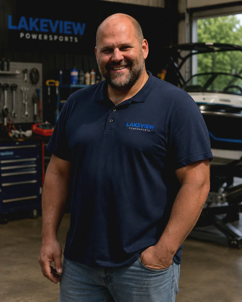 Marko, licensed mechanic at Lakeview Power Sports, in the workshop in front of the shop sign