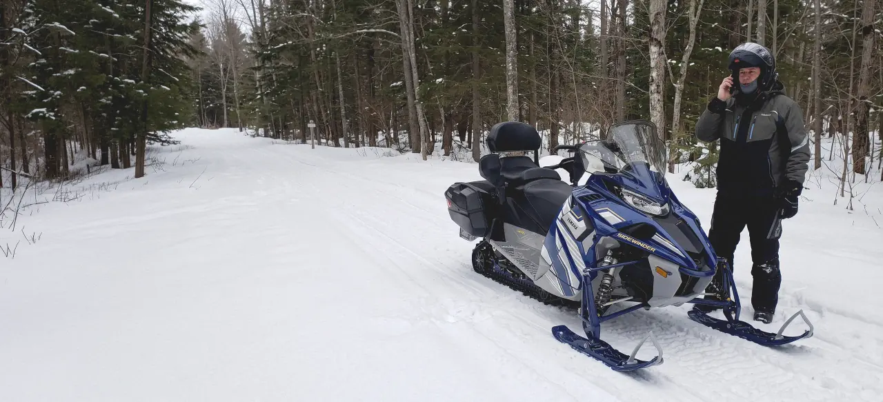 A rider on the phone beside his snowmobile on a snowy Haliburton trail