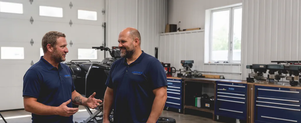 George and Marko talking together on the workshop floor beside an ATV on a lift