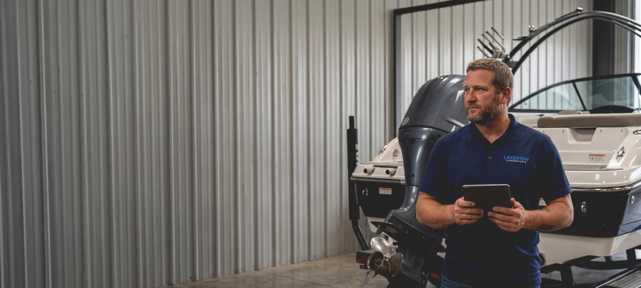 A Lakeview mechanic reading a diagnostic tablet beside a trailered boat and its outboard in the workshop
