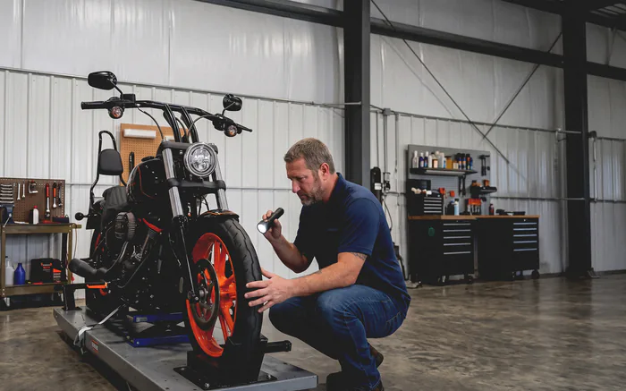 A Lakeview mechanic crouched with a flashlight, inspecting the front wheel and brake of a Harley-Davidson