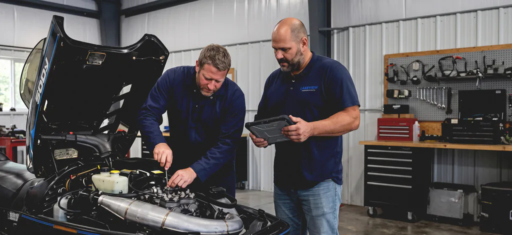 George on the wrench and Marko reading a diagnostic tablet over an open snowmobile engine bay