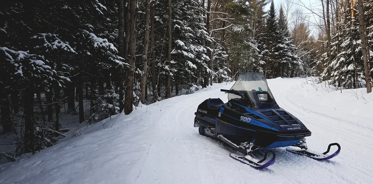 A repaired Polaris sled parked on a groomed trail through snow-covered woods