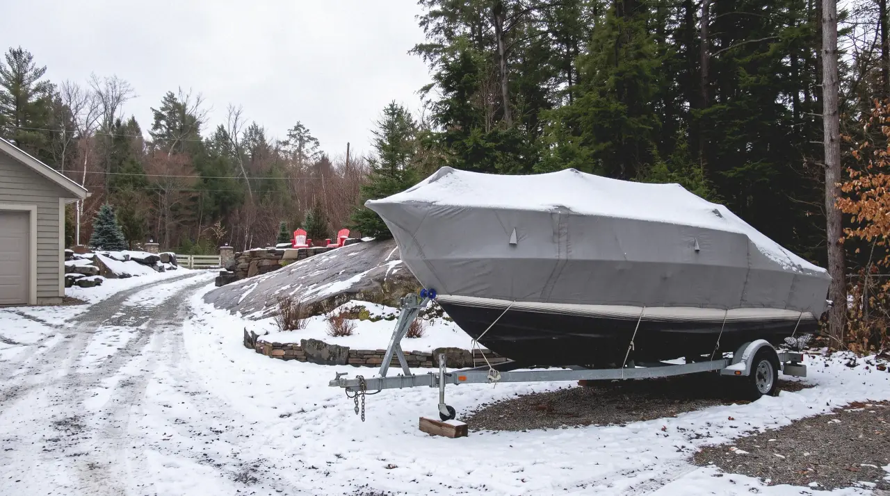 A boat under a fitted cover on its trailer in a snowed-in Haliburton driveway